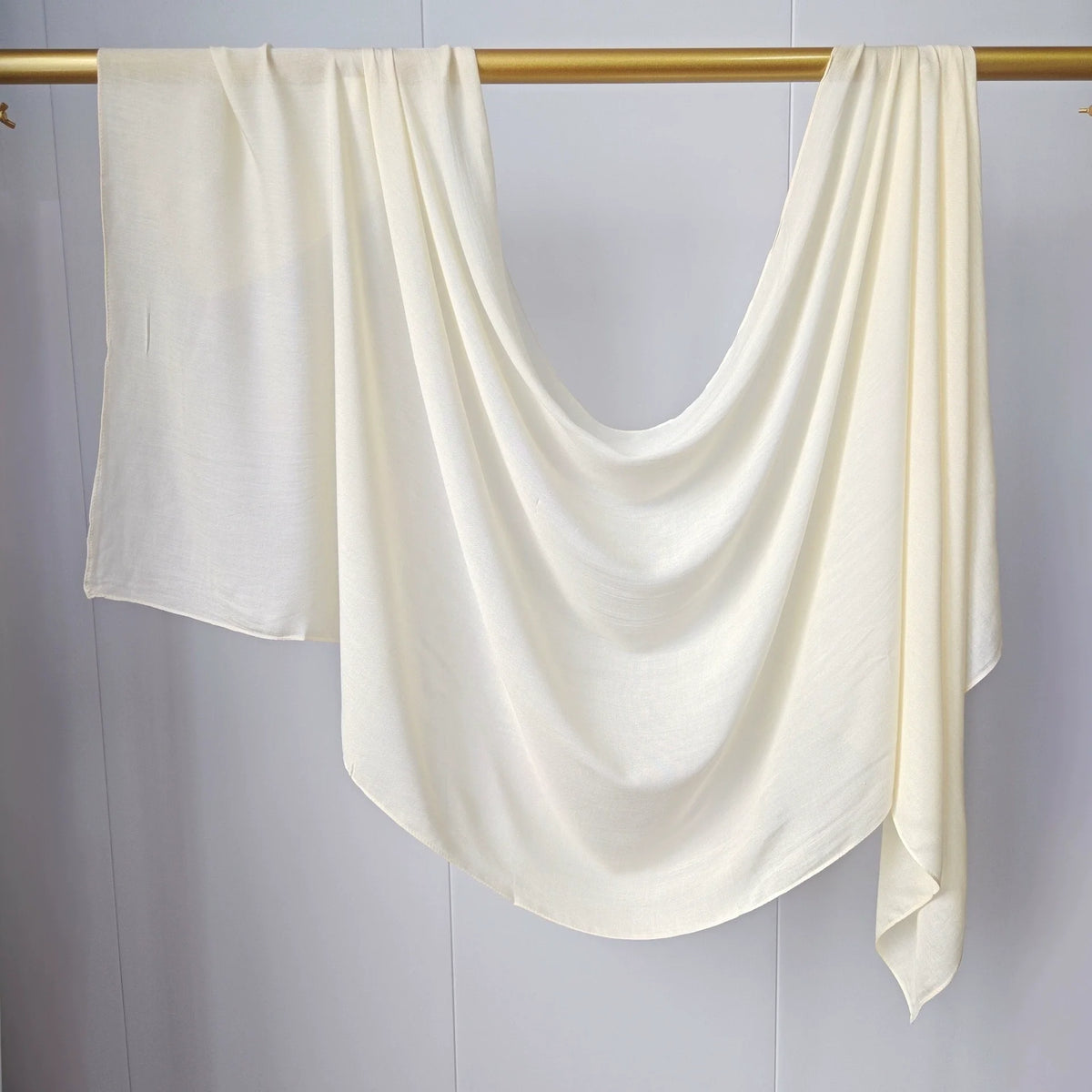 Foulard modal de couleur crème drapé sur un cintre doré sur fond blanc.