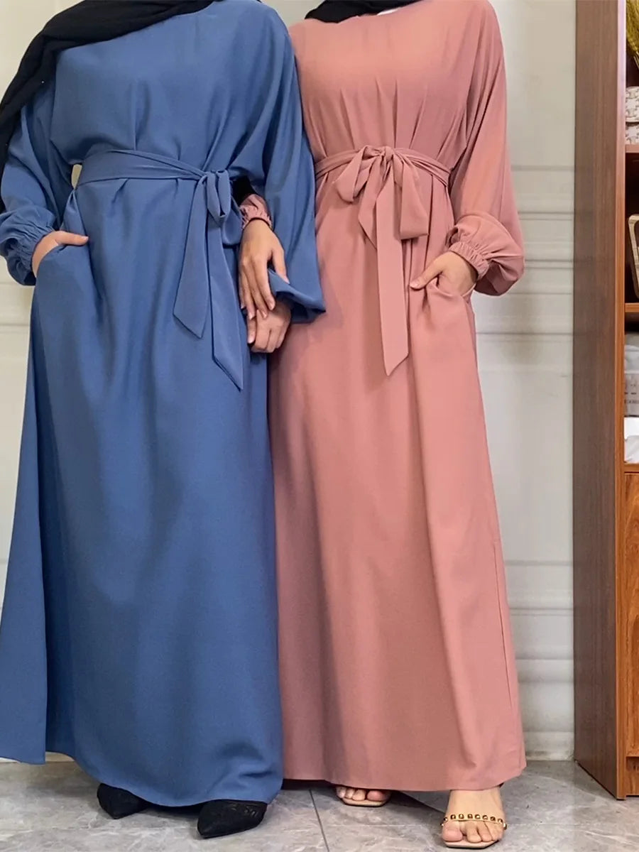 Zwei Frauen in langen Kaftan-Abayas, eine blau und eine rosa, stehen nebeneinander.