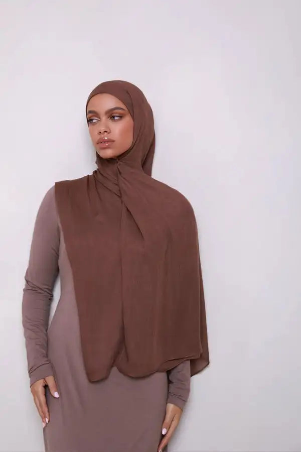 Une femme portant un foulard modal brun uni et une robe à manches longues assortie.