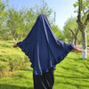 Eine Frau mit dunkelblauem Diamant-Hijab steht draußen in einem grasbewachsenen Park.