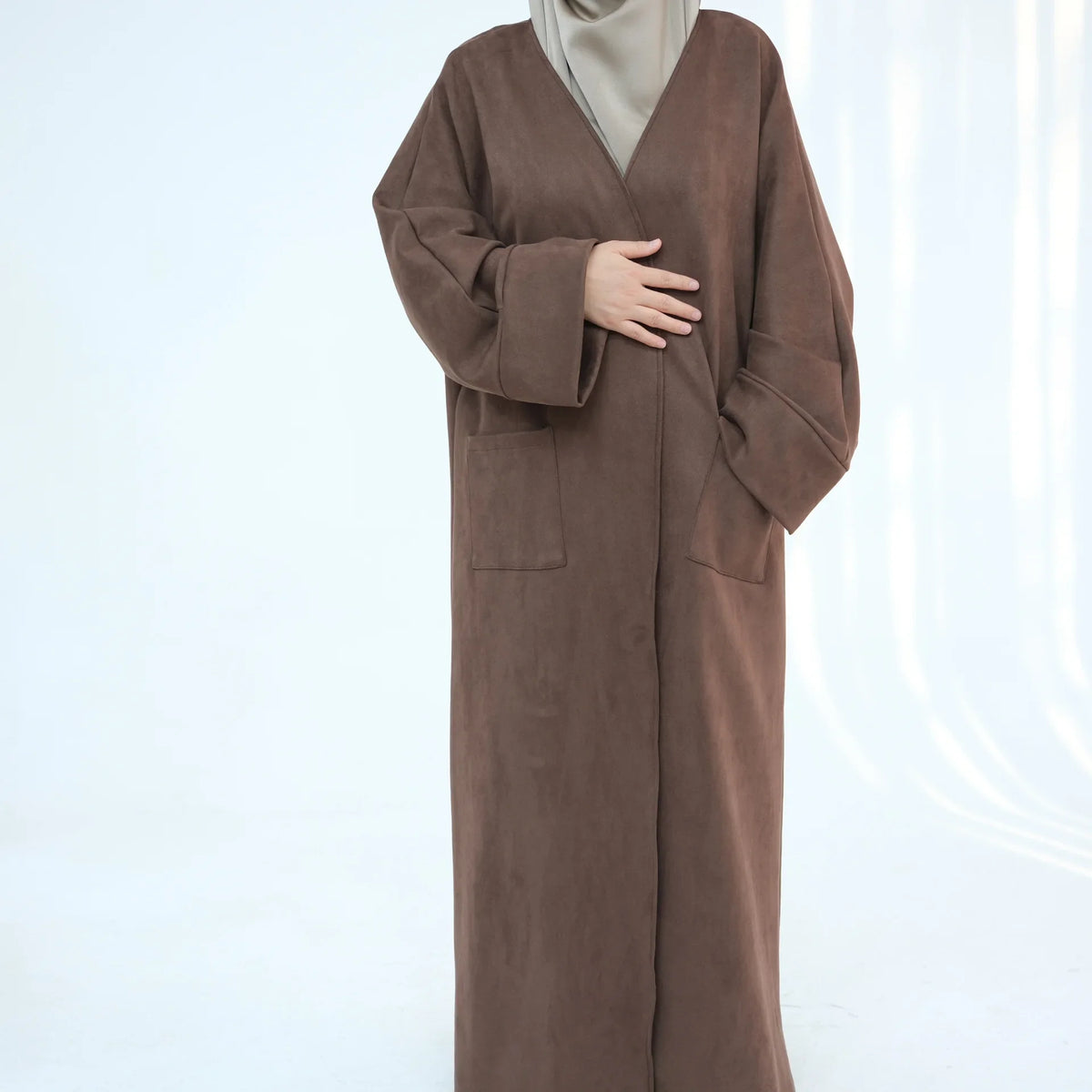 A woman wearing a brown abaya trench coat over a beige hijab.