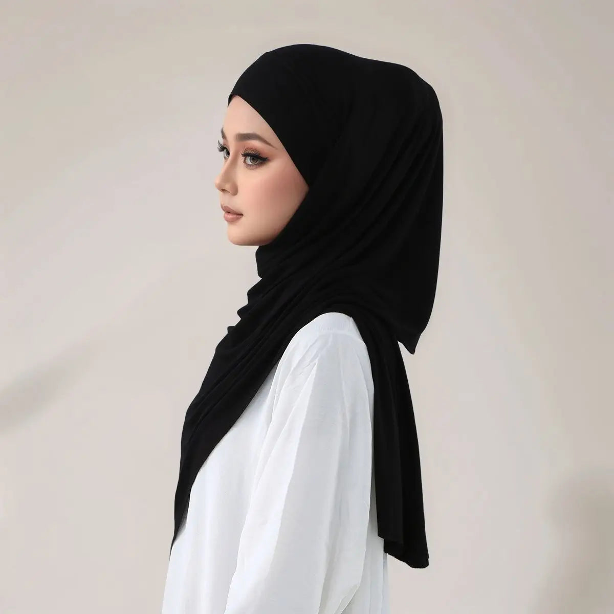 Eine Frau trägt einen schwarzen Instant-Hijab aus elastischem Modaljersey mit Trägern über einem weißen Oberteil.