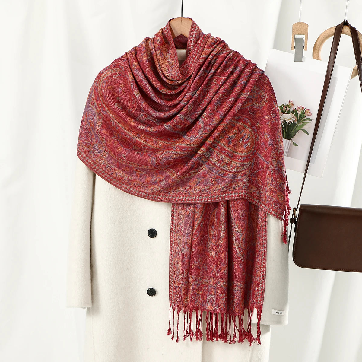 Chal vintage de bordado paisley rojo rosado drapeado sobre un abrigo crema.