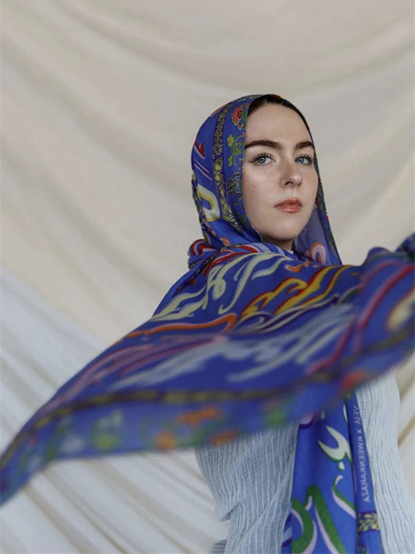 Una mujer vistiendo un pañuelo hiyab estampado de leopardo acuarela azul y morado contra un fondo claro.
