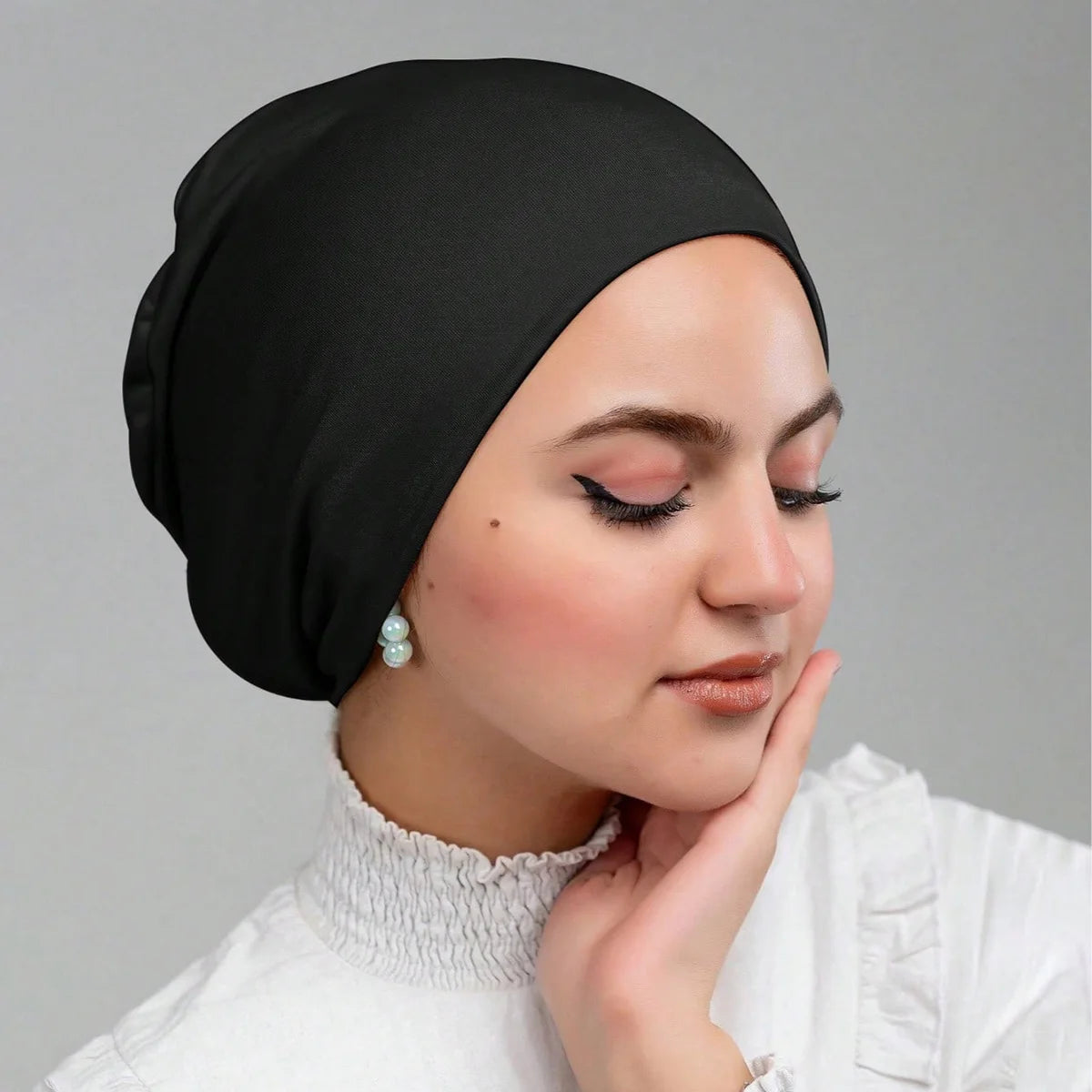 Una mujer vistiendo una gorra de hijab interior de jersey negro, mirando pensativamente hacia abajo.