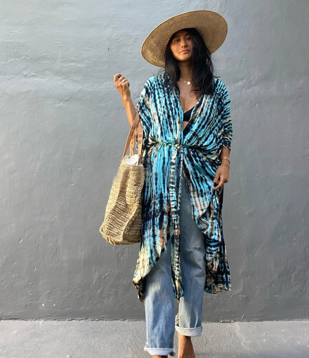Eine Frau trägt einen blau-schwarz gemusterten Kimono-Überwurf über ein Jeans-Outfit, mit Strohhut und einer geflochtenen Tas