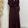 Eine Frau trägt eine lange, maroonfarbene fließende Abaya Kaftan mit weißem Hijab.
