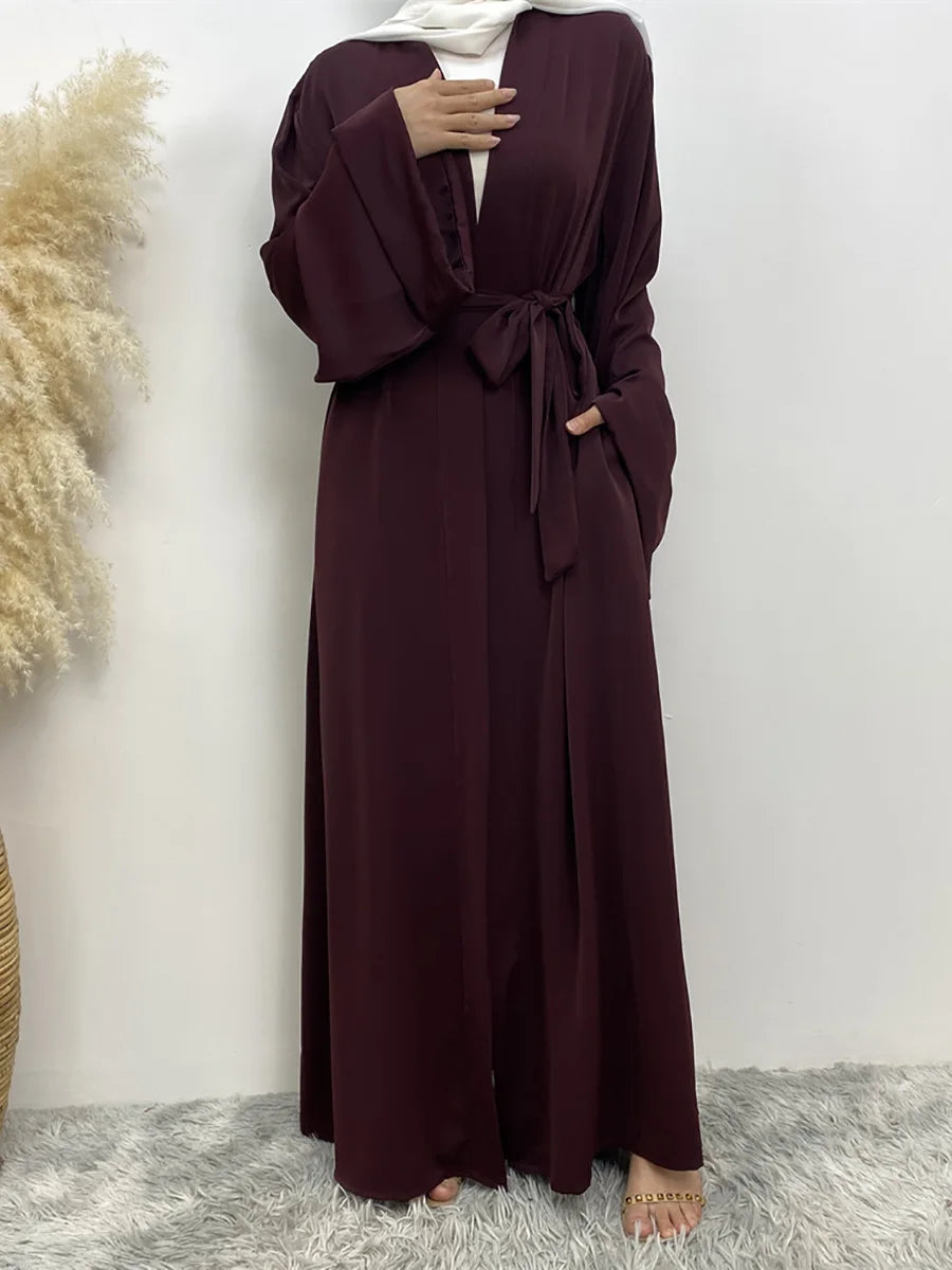 Eine Frau trägt eine lange, maroonfarbene fließende Abaya Kaftan mit weißem Hijab.