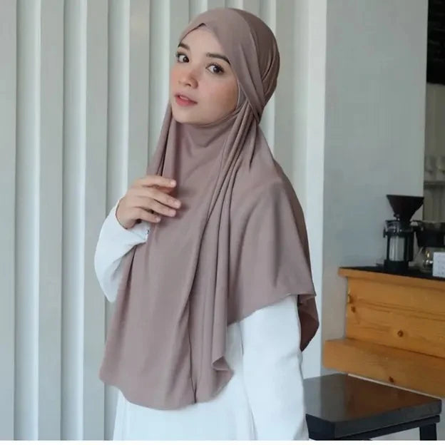 Eine Frau trägt einen großen, einfachen braunen ethnischen Schal als Hijab und weiße Kleidung.