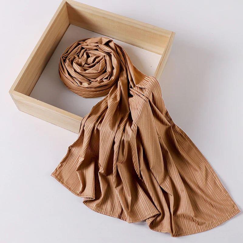 A tan ribbed jersey hijab scarf is draped over a light wooden frame.