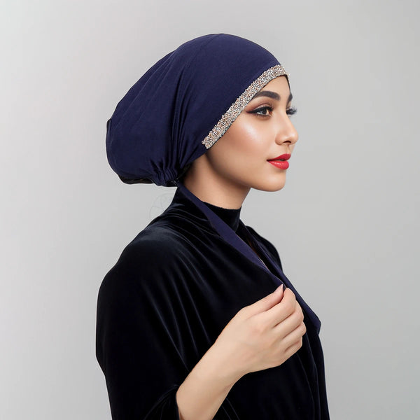 امرأة ترتدي حجاب مخمل أزرق داكن مزين بحافة من أحجار الراين المتلألئة وبلوزة متناسقة.