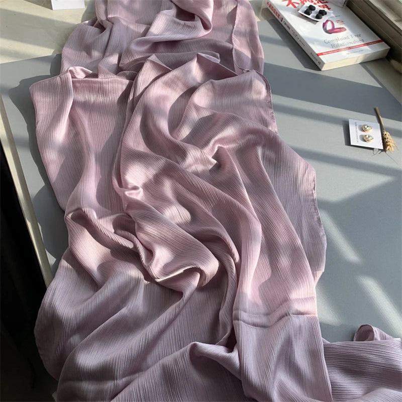 Fließender hellrosa crinkliger Satin-Chiffon-Hijab drapiert auf einer Oberfläche neben einer Box.