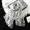 Ein weißer Polka-Dot-Schal über einem schwarzen Hintergrund neben einem schwarzen Rahmen und einer goldenen Kette.