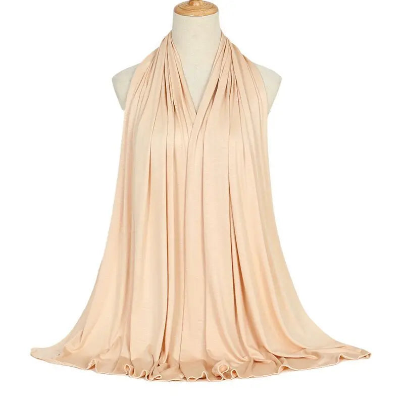 Un pañuelo de algodón modal color melocotón pálido y fluído drapeado alrededor del cuello de un maniquí.