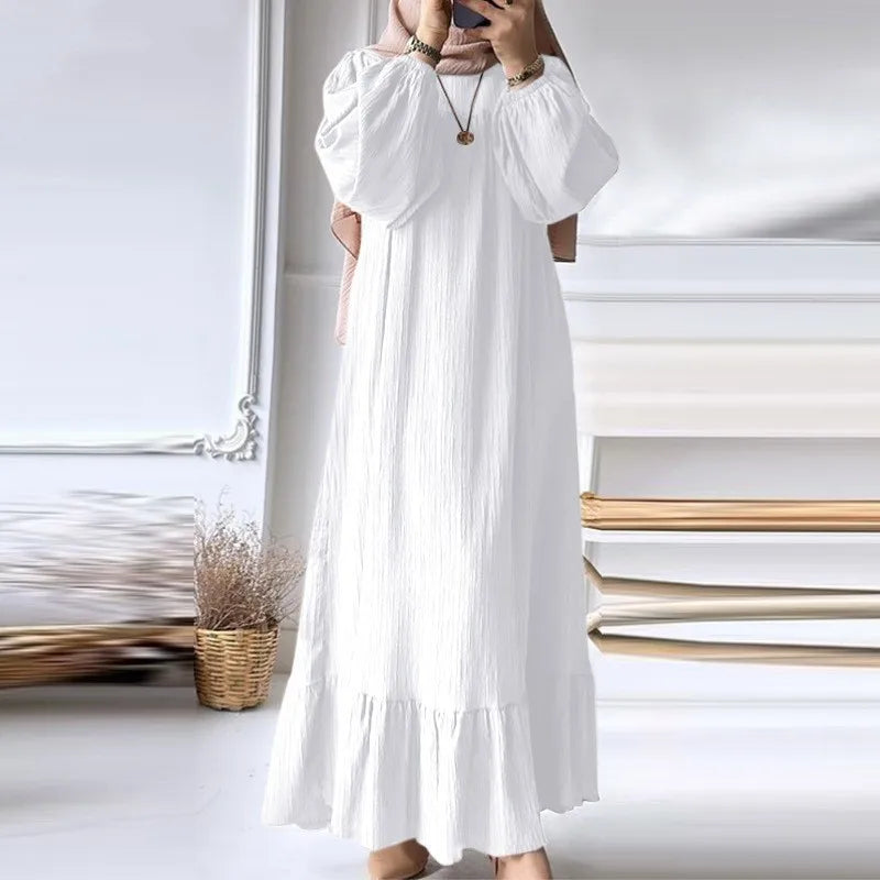 Une femme portant une longue robe maxi bohème blanche à manches et à ourlet froncés, debout à l'intérieur.