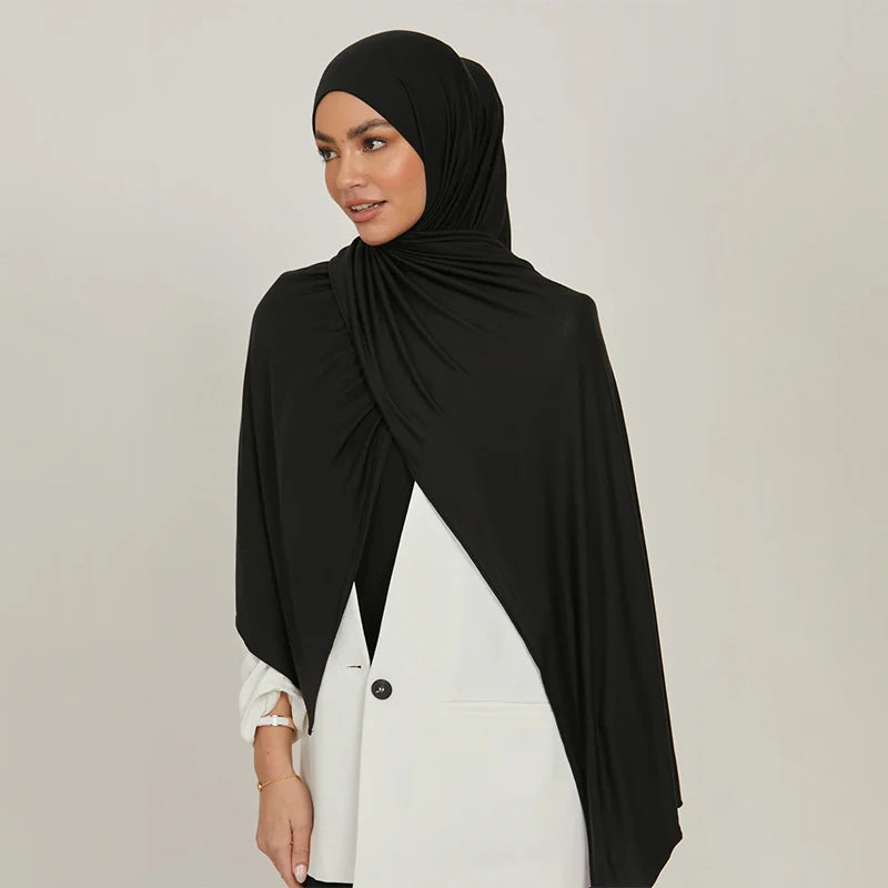 A woman wearing a black stretchy jersey plain hijab scarf and a white top.