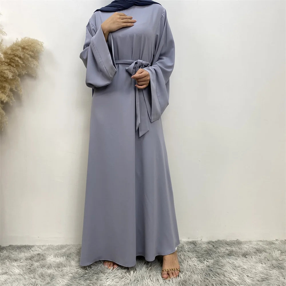 Eine Frau in einem eleganten, bodenlangen grauen Maxi-Abaya und einem dunkelblauen Hijab.