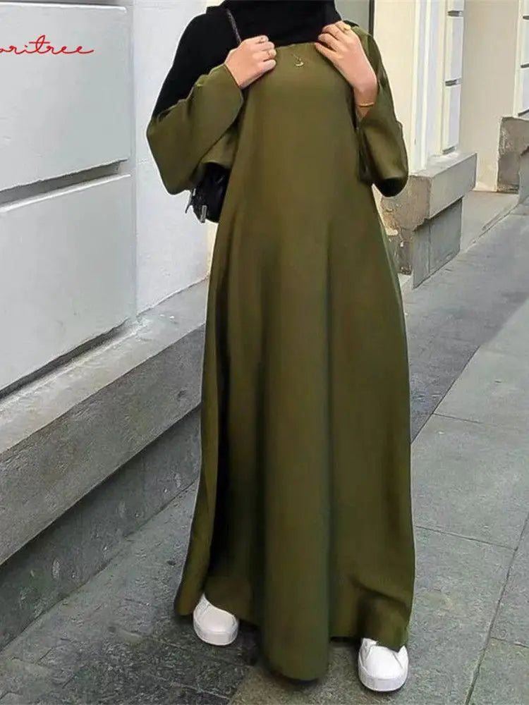 Eine Frau trägt eine fließende olivgrüne Abaya mit weiten Ärmeln und weißen Schuhen.