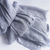Une pile de foulards hijab en coton viscose gris doux avec pompons, pliés sur une surface blanche.