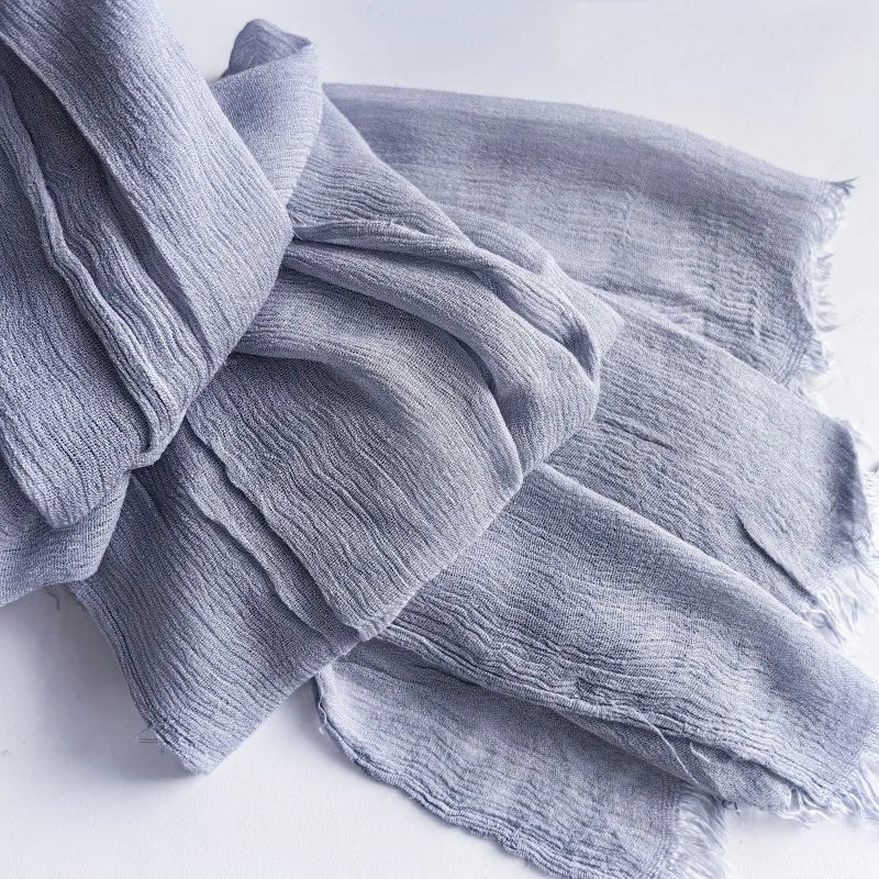 Une pile de foulards hijab en coton viscose gris doux avec pompons, pliés sur une surface blanche.