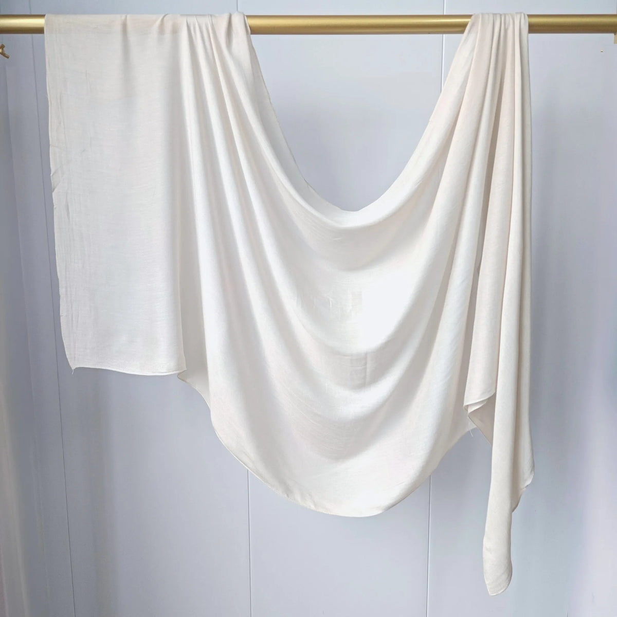 Foulard modal uni blanc drapé sur une tige dorée sur fond clair.