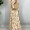 Una mujer vistiendo una elegante caftán de abaya floral y llevando un bolso tejido beige.