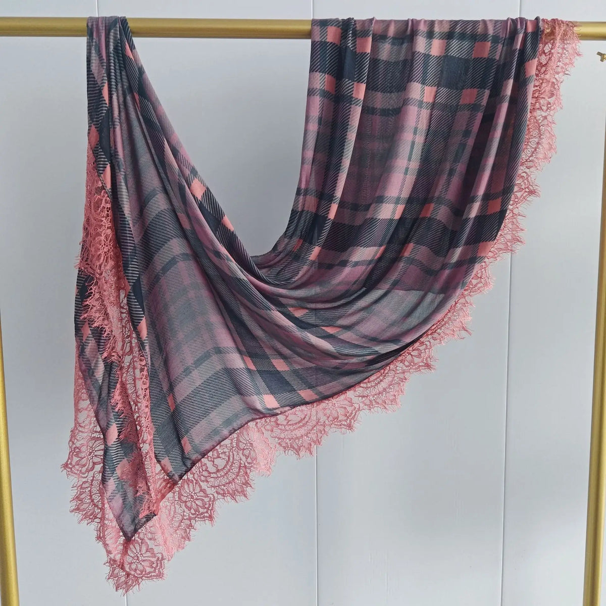 A draped plaid hijab scarf in shades of pink and charcoal gray with delicate lace trim.