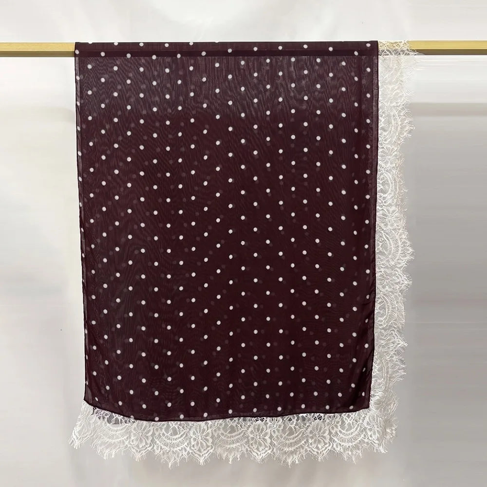 Hijab de encaje marrón oscuro con estampado doble y colgando contra un fondo claro.