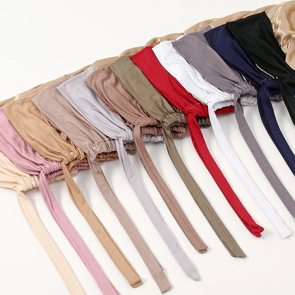 A collection of satin hijab caps and undercaps in various shades including pink, beige, gray, red, and navy.