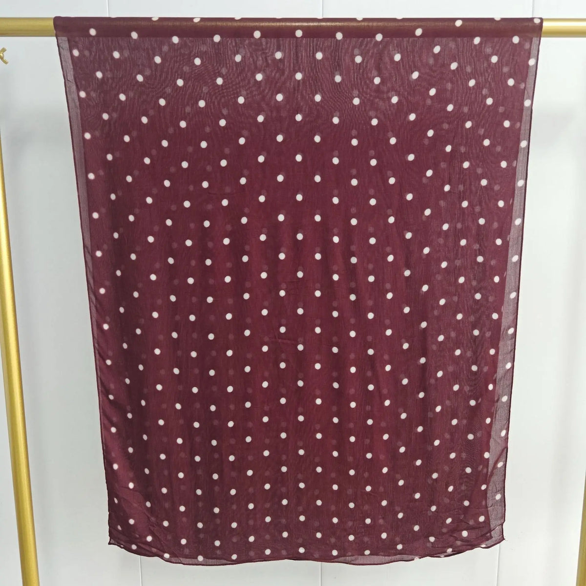 Ein tiefburgunder, durchscheinender Schal mit kleinen weißen Polka Dots vor hellem Hintergrund.