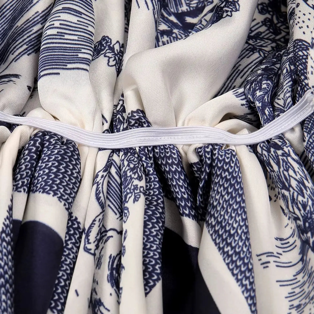 A close-up of an elegant satin silk instant hijab scarf featuring a blue and white patterned fabric gathered with a white tie