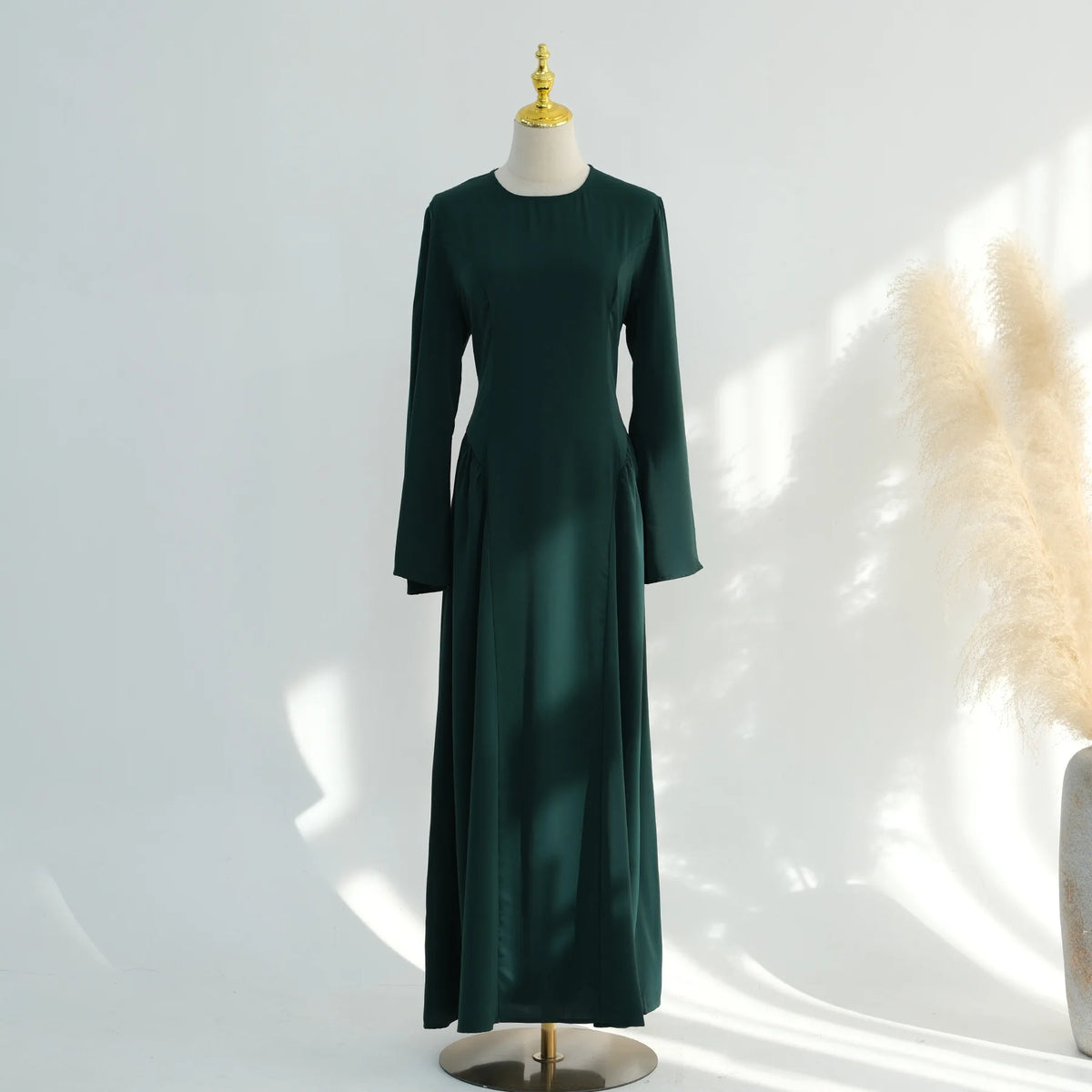 Una abaya de color verde esmeralda oscuro, de largo, mostrada en maniquí.