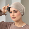 A woman is adjusting a beige elastic headband hijab cap on her head.