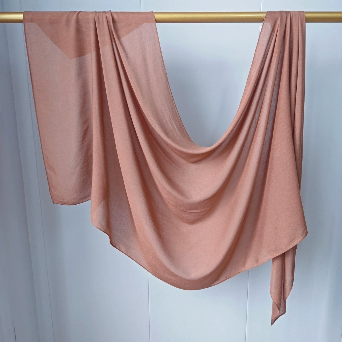 Foulard modal couleur pêche fluide et solide drapé sur une tige dorée.