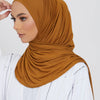 Eine Frau trägt einen einfarbigen braunen Jersey-Hijab und weiße Kleidung.