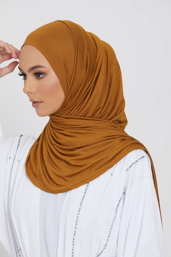 A woman wearing a solid brown jersey hijab scarf and white clothing.