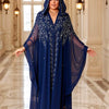 Una mujer modela un largo y fluido vestido maxi abaya azul marino con mangas de murciélago en un elegante entorno interior.