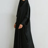 Eine Frau in einer schwarzen, bedeckenden Abaya mit gerafften Ärmeln vor weißem Hintergrund.