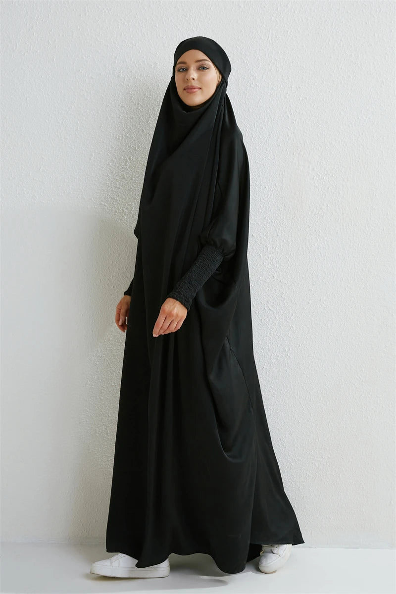 Eine Frau in einer schwarzen, bedeckenden Abaya mit gerafften Ärmeln vor weißem Hintergrund.
