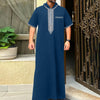 A man wearing a navy blue Moroccan ethnic thobe with a stand collar and silver embroidery.