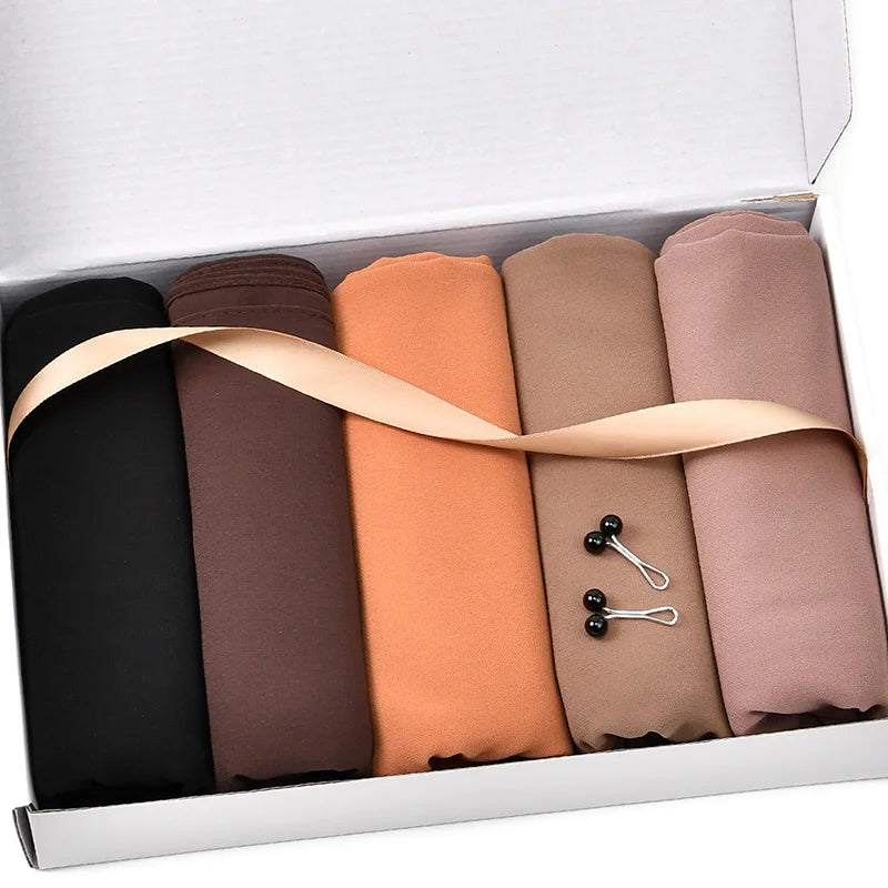 Un juego de cuatro pañuelos de chifón de colores sólidos en negro, marrón, naranja y malva, empaquetados en una caja blanca.