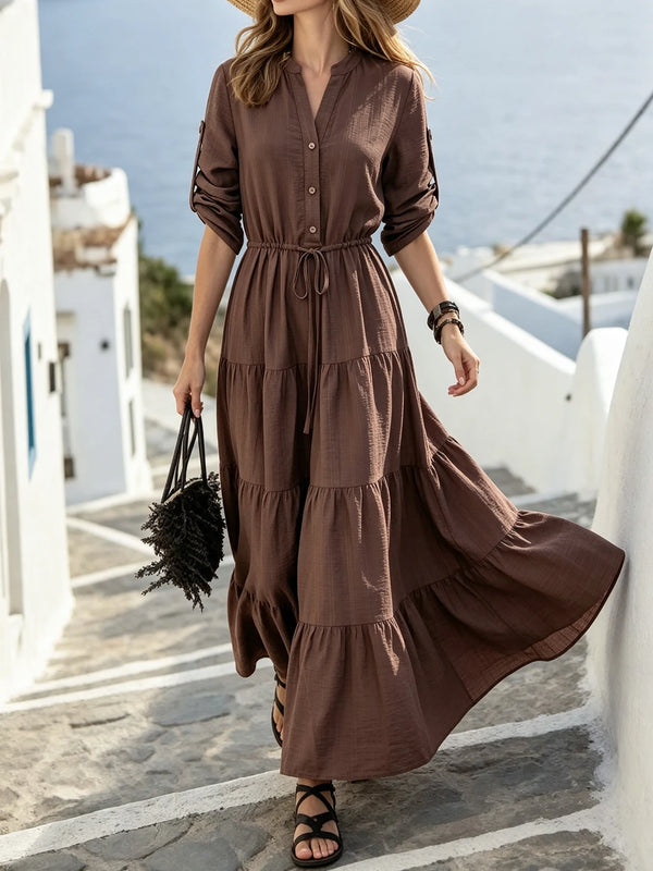 A woman wearing a brown maxi dress with a drawstring waist and ruffle hem walking outdoors.
