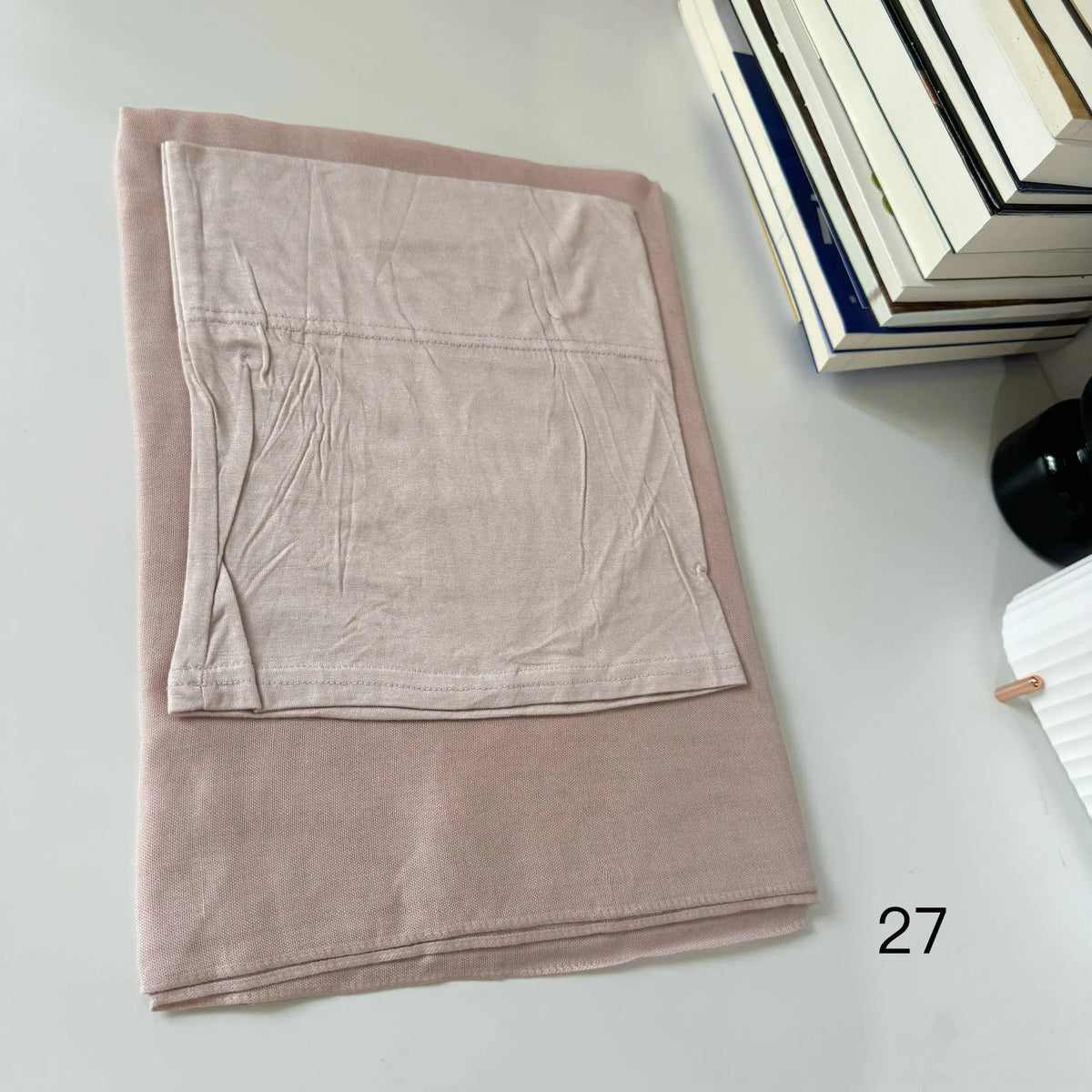 A folded soft pink hijab set made of modal rayon fabric resting on a white surface.