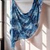 Blau-weißes Aquarell-Blumenmuster-Poncho, drapiert an einer weißen Wand.