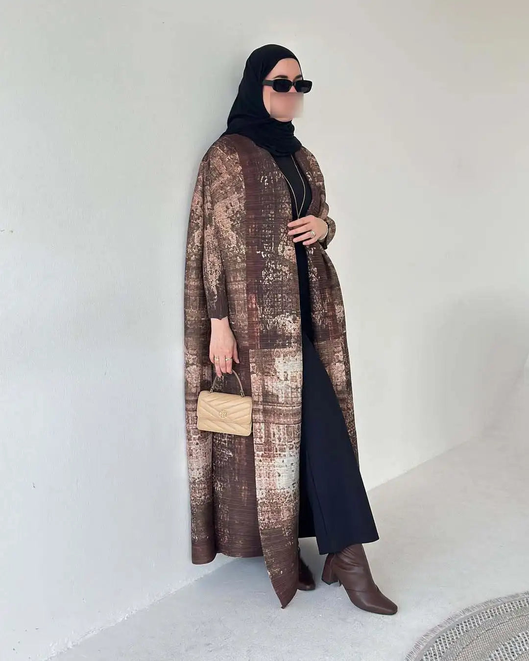 Una mujer vistiendo un cárdigan abaya de patrón marrón y ropa negra, mirando a un lado.