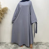 Una abaya gris larga y fluida para mujeres con hijab negro y detalles de borlas.