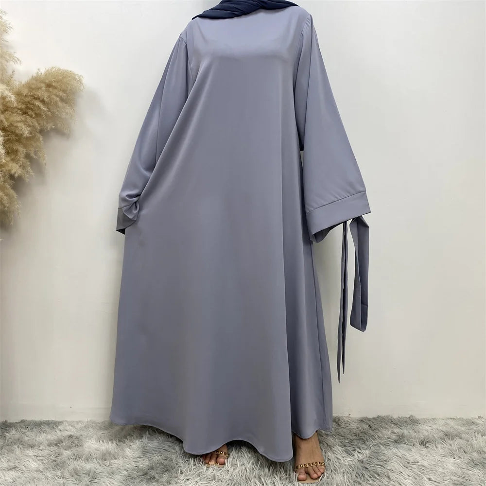 Una abaya gris larga y fluida para mujeres con hijab negro y detalles de borlas.