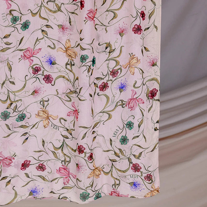 A close-up of a light pink watercolor printed scarf featuring green and pink floral vines.