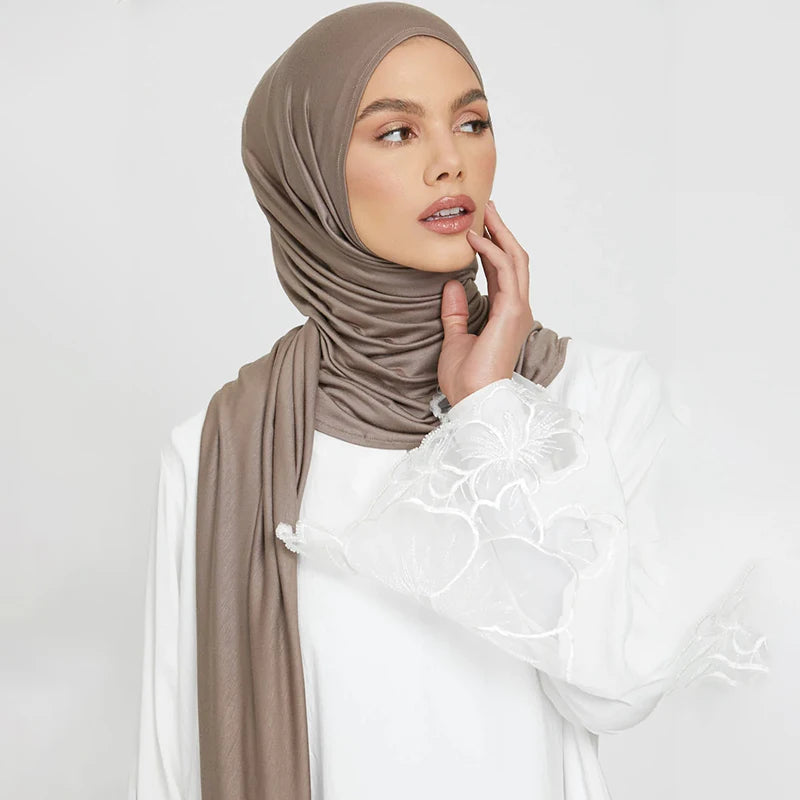 A woman wearing a solid taupe stretchy jersey plain hijab scarf and white top.