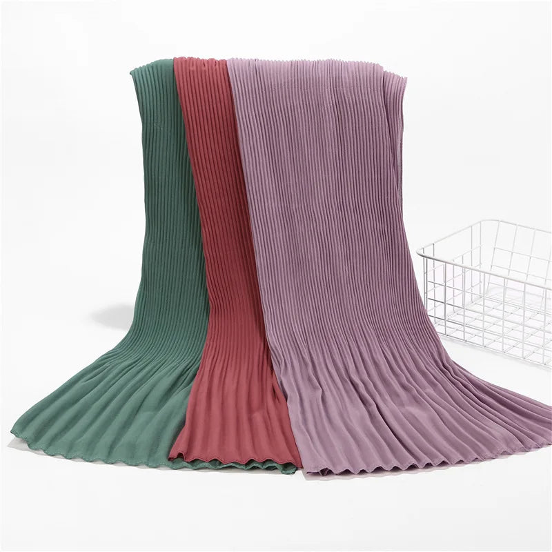 Ein Stapel von Crinkle-Chiffon-Hijabs in Grüntönen, Pink und Mauve.